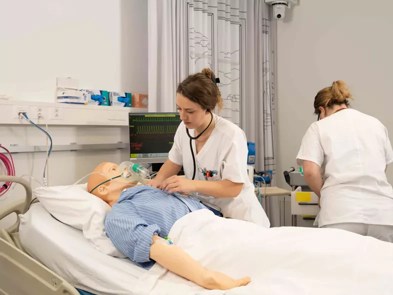 Deux étudiantes infirmières en simulation, l'une ausculte un mannequin haute fidélité