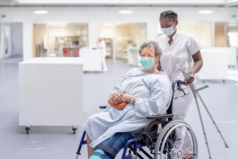 Etudiante infirmière pousse patiente simulée en fauteuil roulant